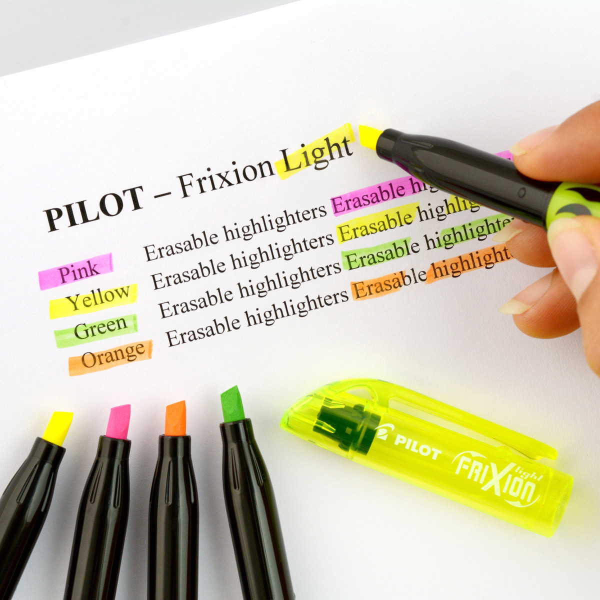 Hand using a yellow PILOT FriXion Light erasable highlighter on text with open pink, orange and green erasable highlighters on page. 