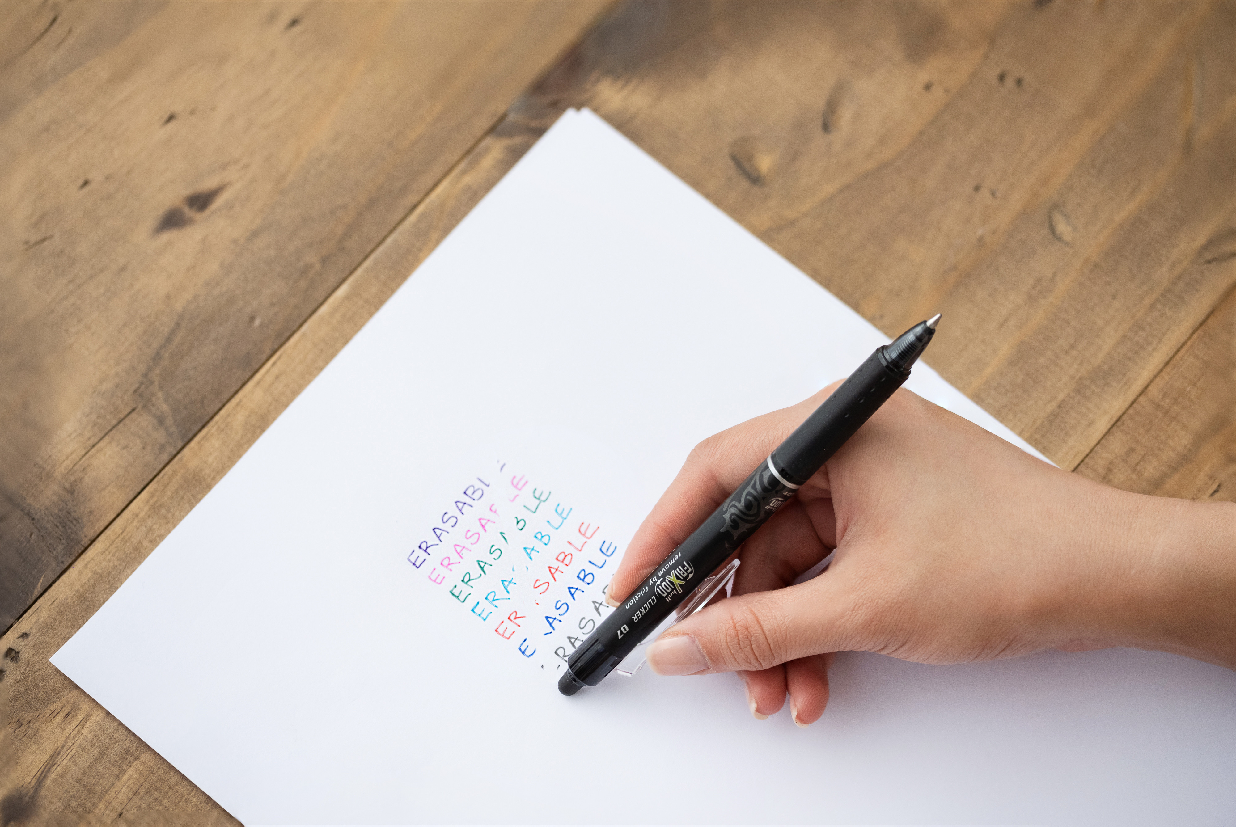 Pilot FriXion Clicker Black pen being used to erase the word 'erasable' that is written in different colours on paper.