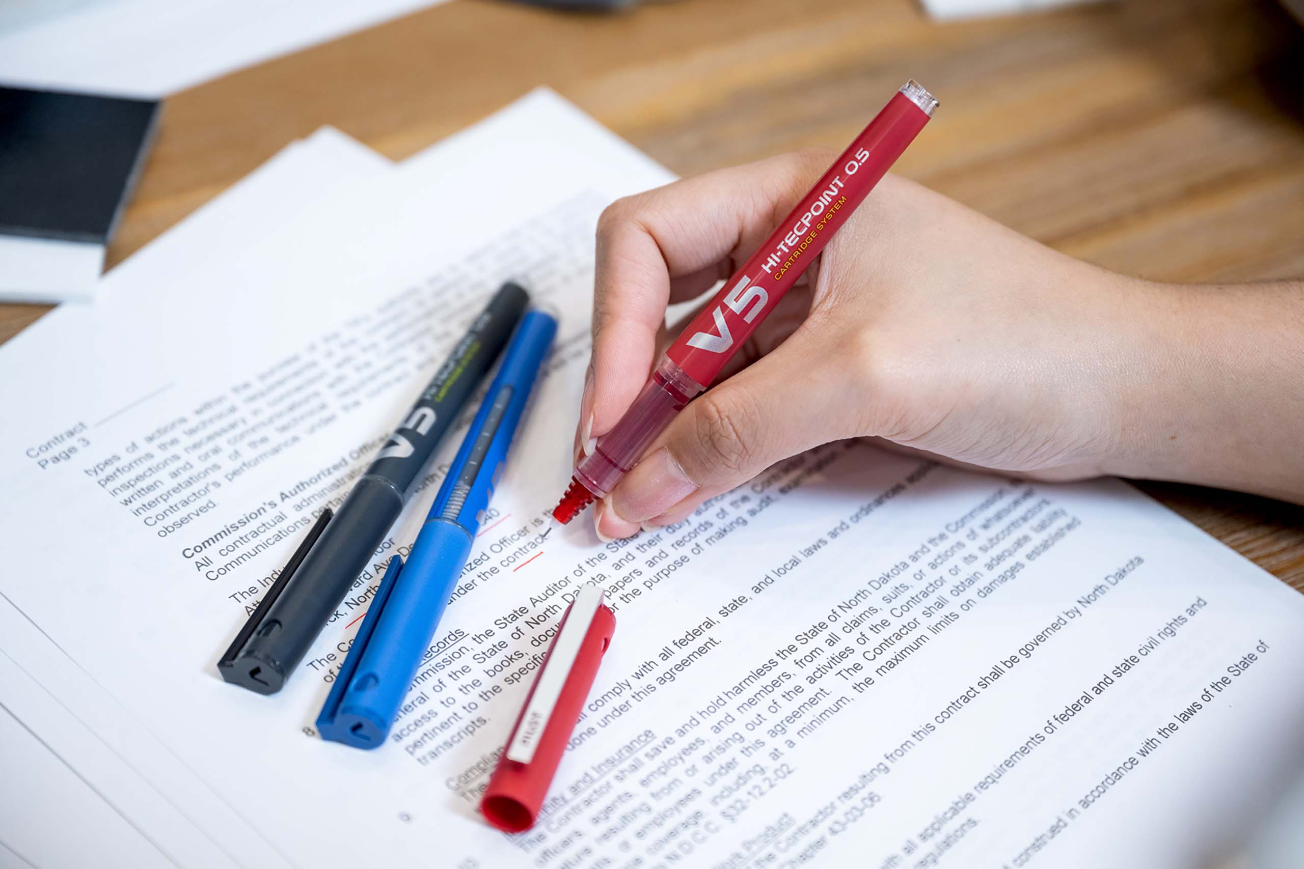 Woman using a red Pilot Hi-Tecpoint V5 pen to underline text on a document.