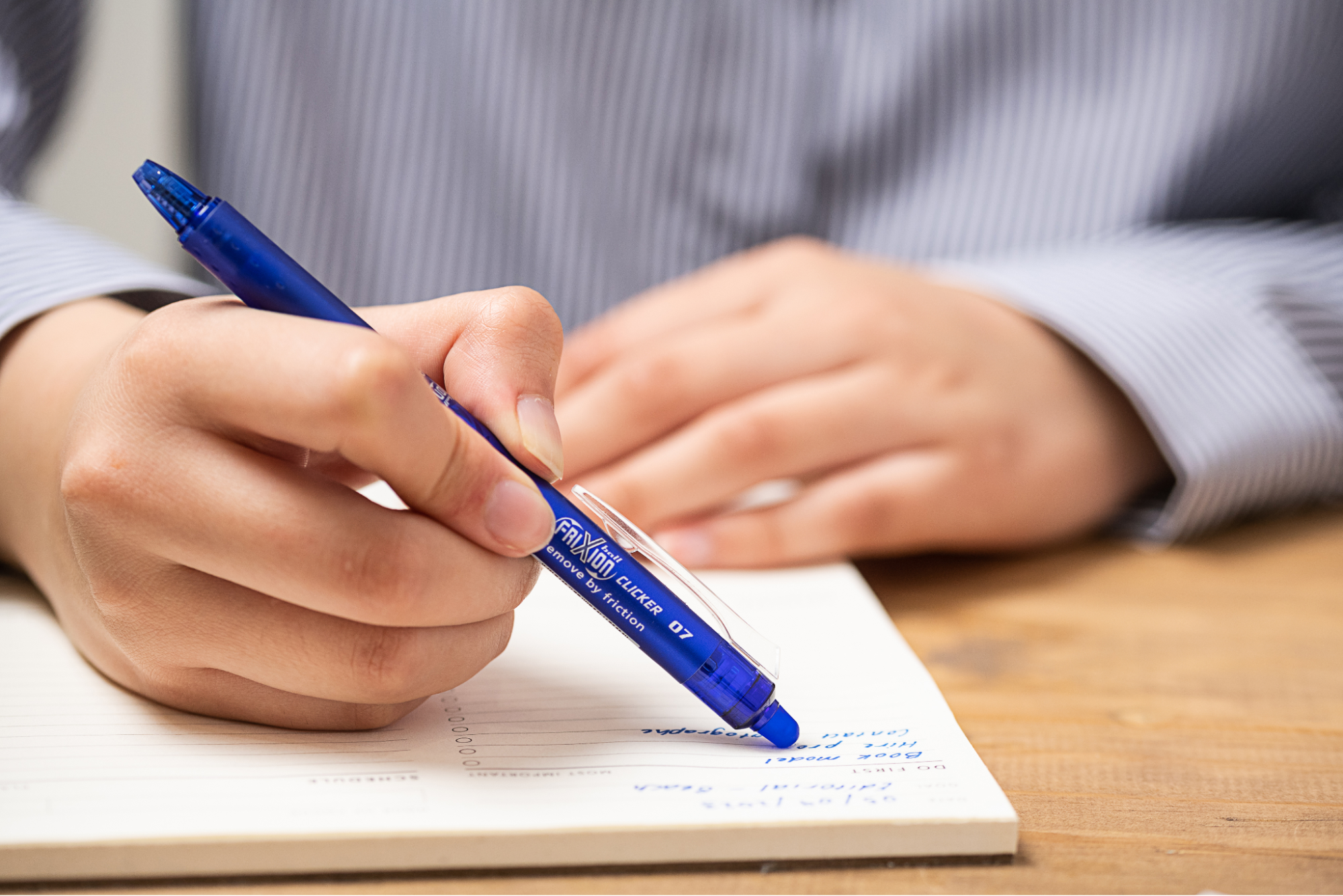 Close-up of a hand writing in a lined notebook with a blue Pilot FriXion pen—one of the best pens for writing