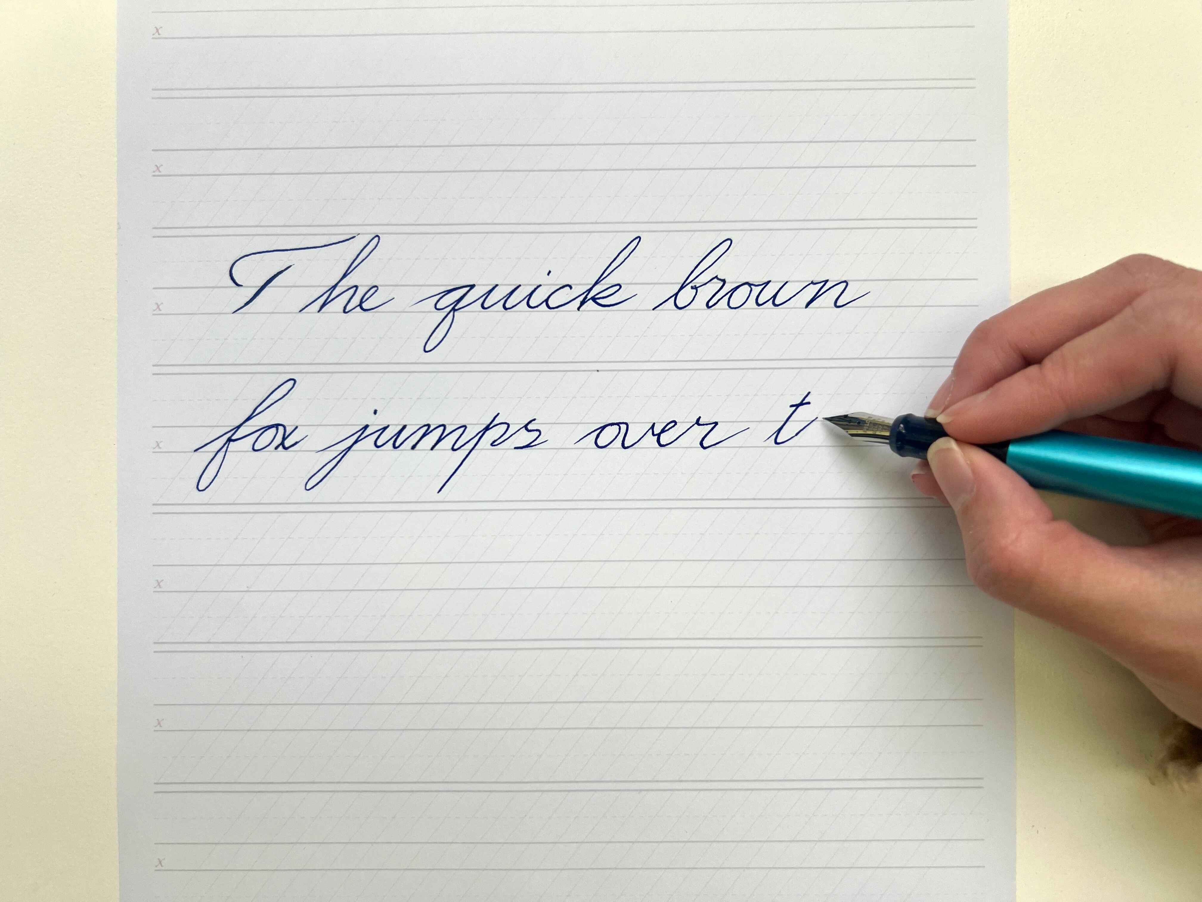 Woman practising fountain pen calligraphy, writing the words “The quick brown fox jumps over t…” 