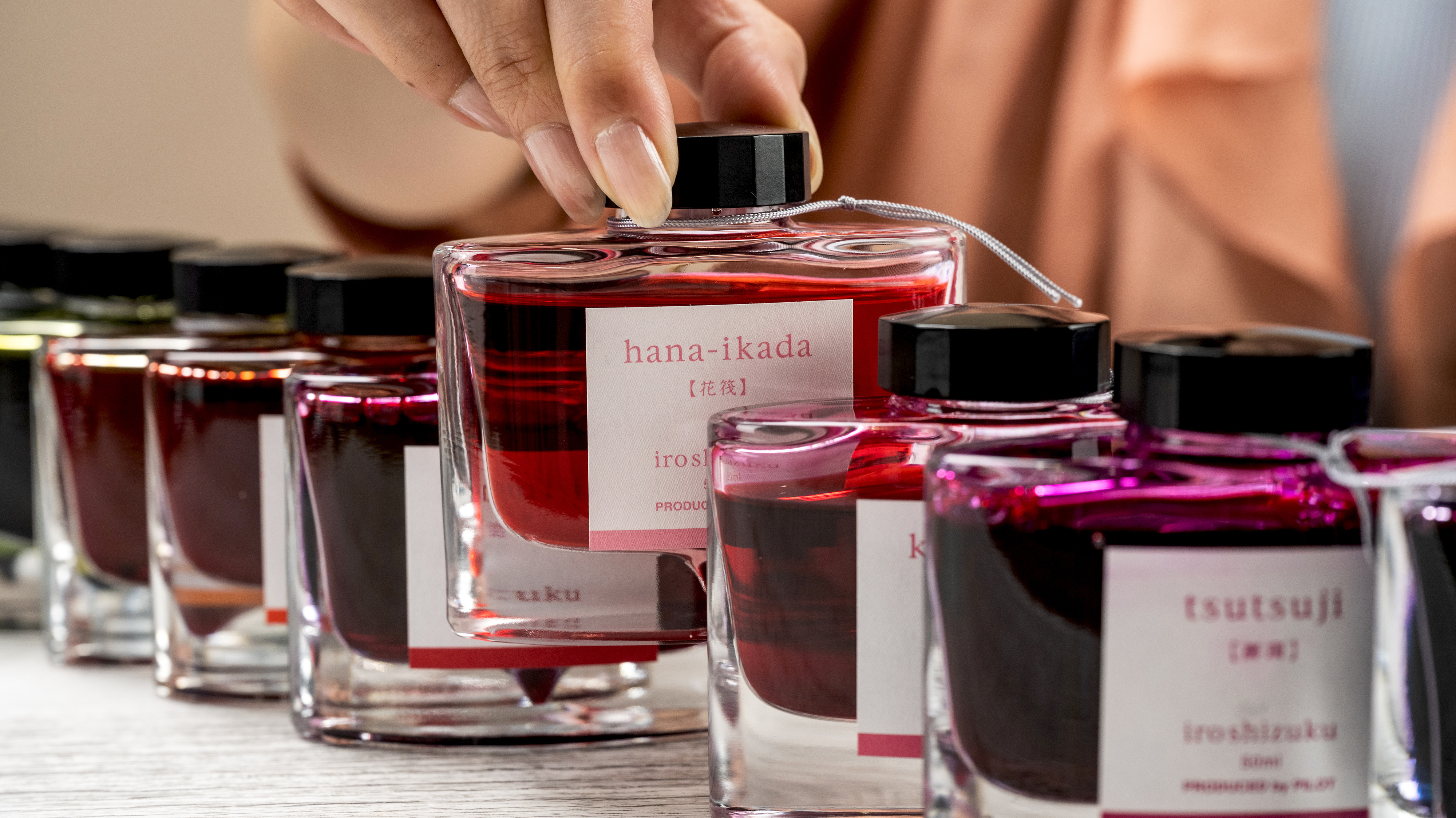 Close up on a woman's hand selecting the hana-ikada shade from a section of iroshizuku Fountain Pen Ink Bottle.