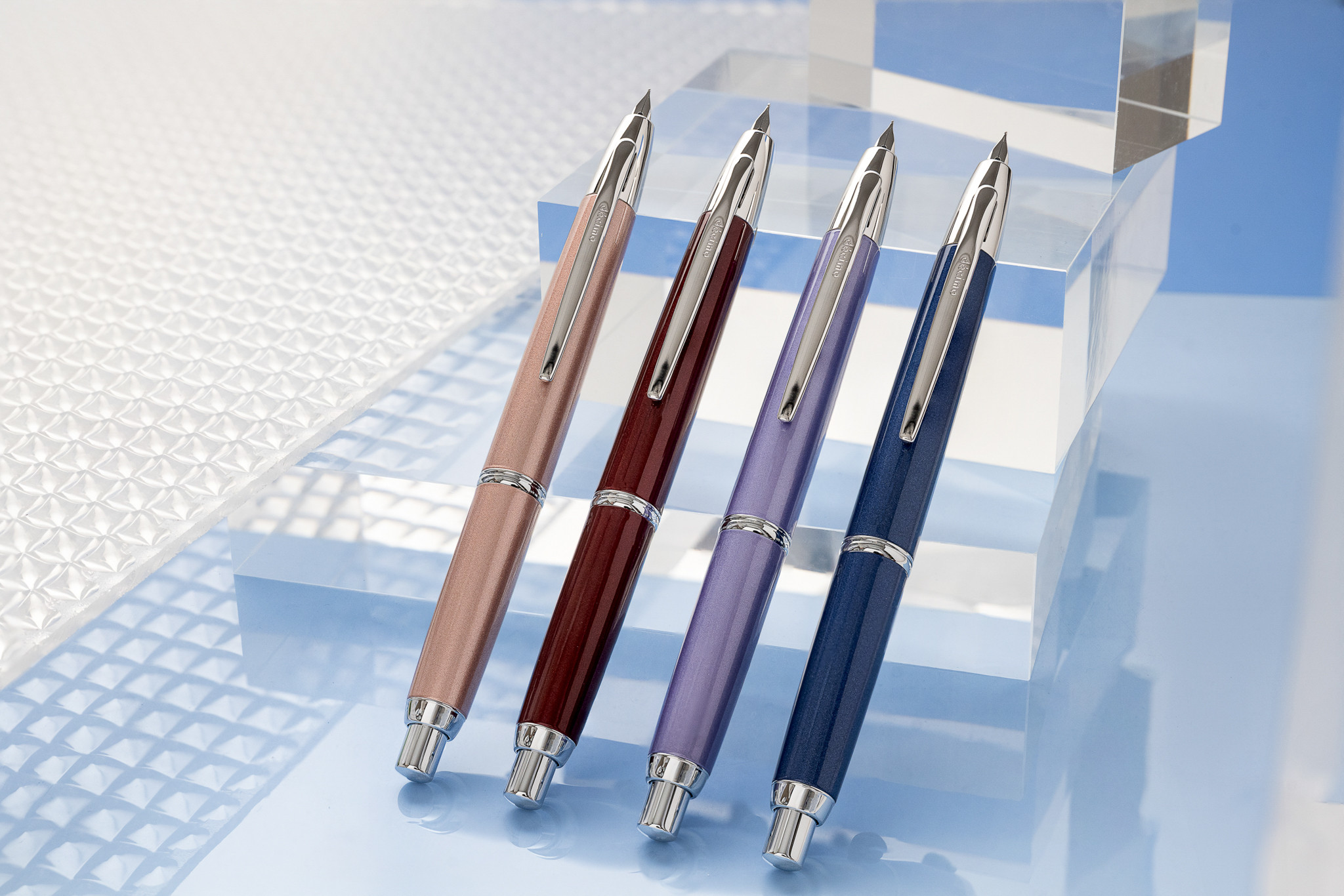 Four Pilot Capless Decimo fountain pens in champagne pink, red, violet, and navy displayed on a clear acrylic stand
