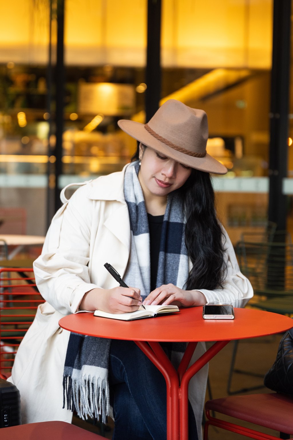 Woman writing with pen and paper at a café table, choosing analogue tools over digital in a modern setting.