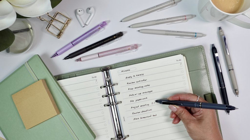Mariane Cresp writing in her planner with a FriXion pen beside a coffee cup on her desk.