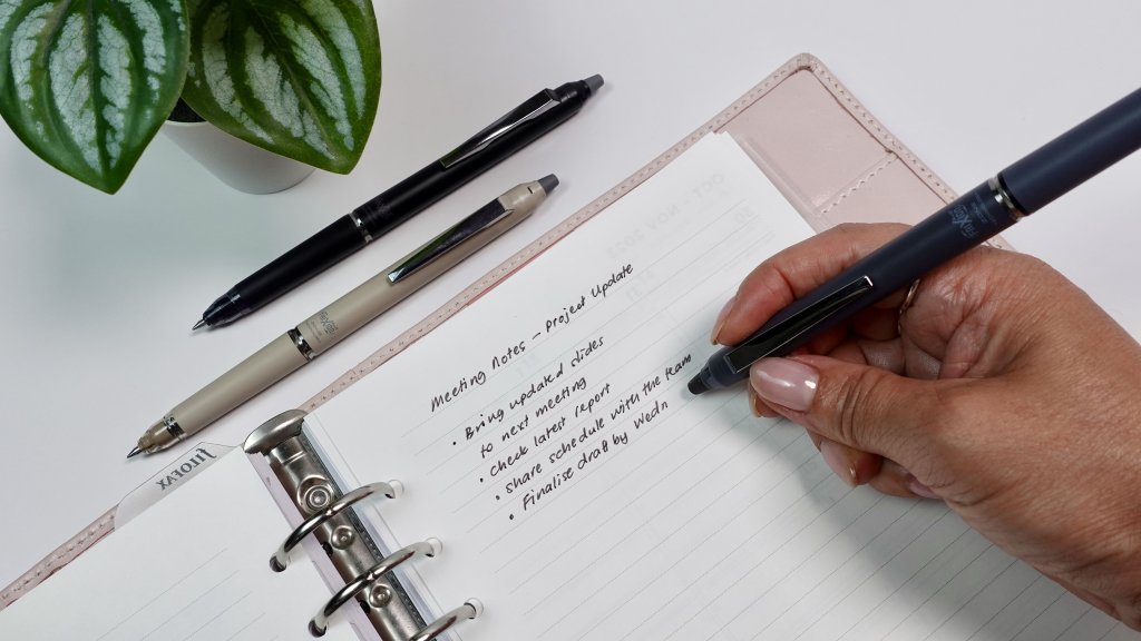 A FriXion pen erasing black ink from a planner page, showing the clean erasable feature in action.