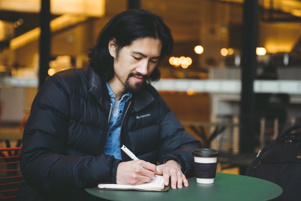 man sitting at a café mindfully writing down yearly goals with his premium fountain pen.